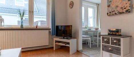 A modern living room with a TV, white furniture, a radiator, and a view of the outside.