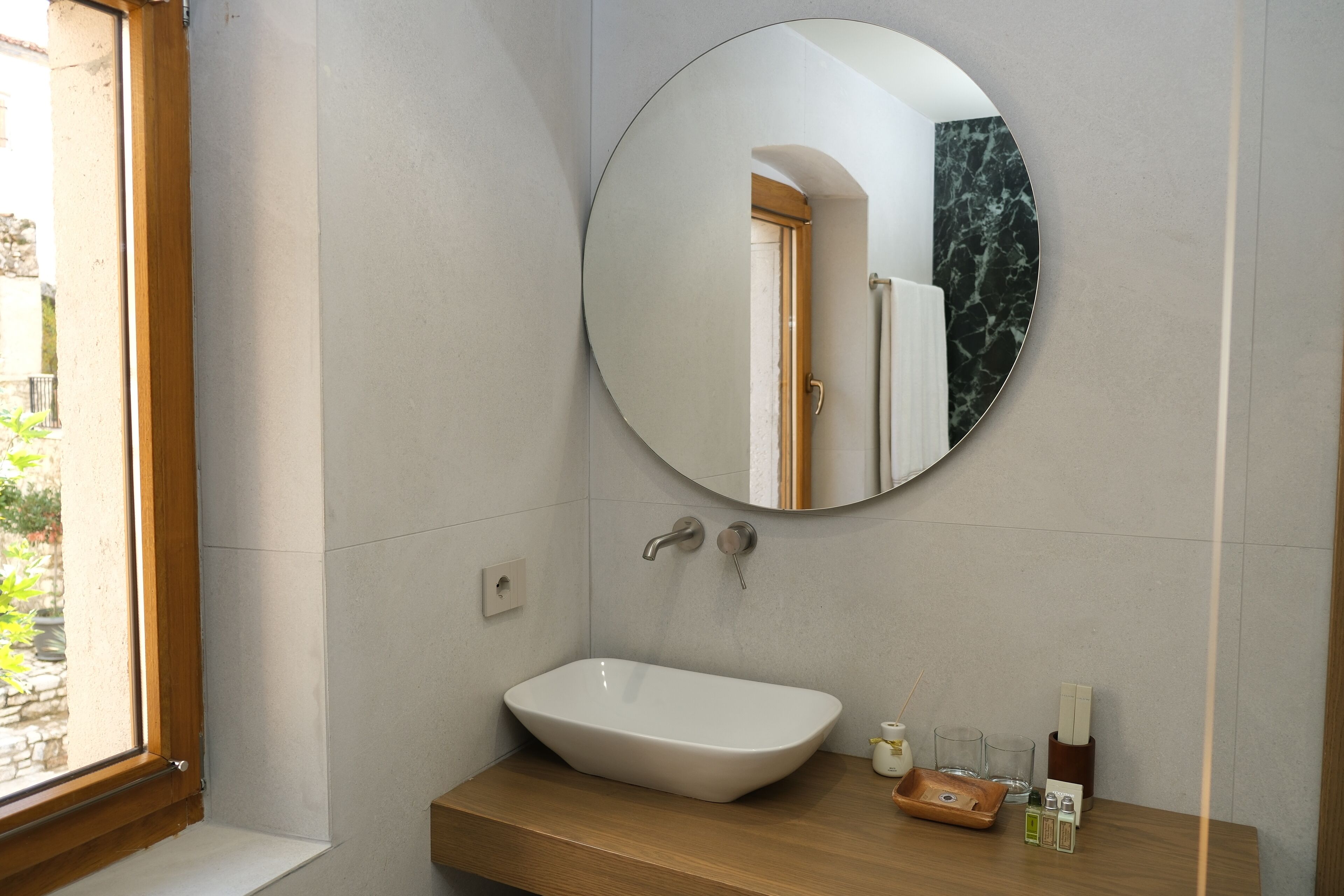 A bathroom with a round mirror, a white sink, and a wooden countertop.