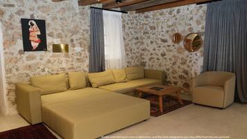 Uma sala de estar com sofá, mesa de centro de madeira, cadeira, quadro e parede de pedra.
