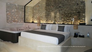 Una camera da letto moderna con parete in pietra, un letto grande, una vasca da bagno e lampade a sospensione.