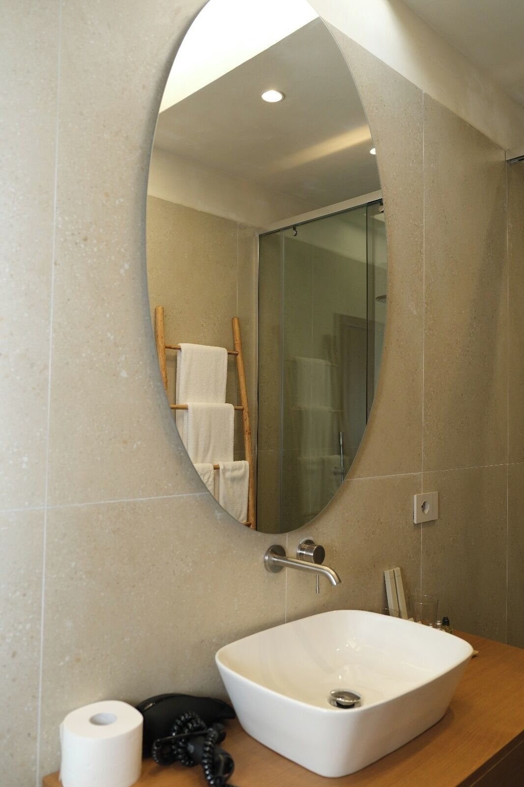 Un baño con un espejo ovalado grande, un lavabo blanco y una cabina de ducha con paredes de vidrio.