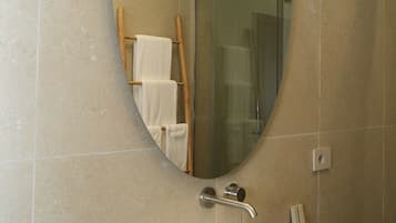 Un baño con un espejo ovalado grande, un lavabo blanco y una cabina de ducha con paredes de vidrio.