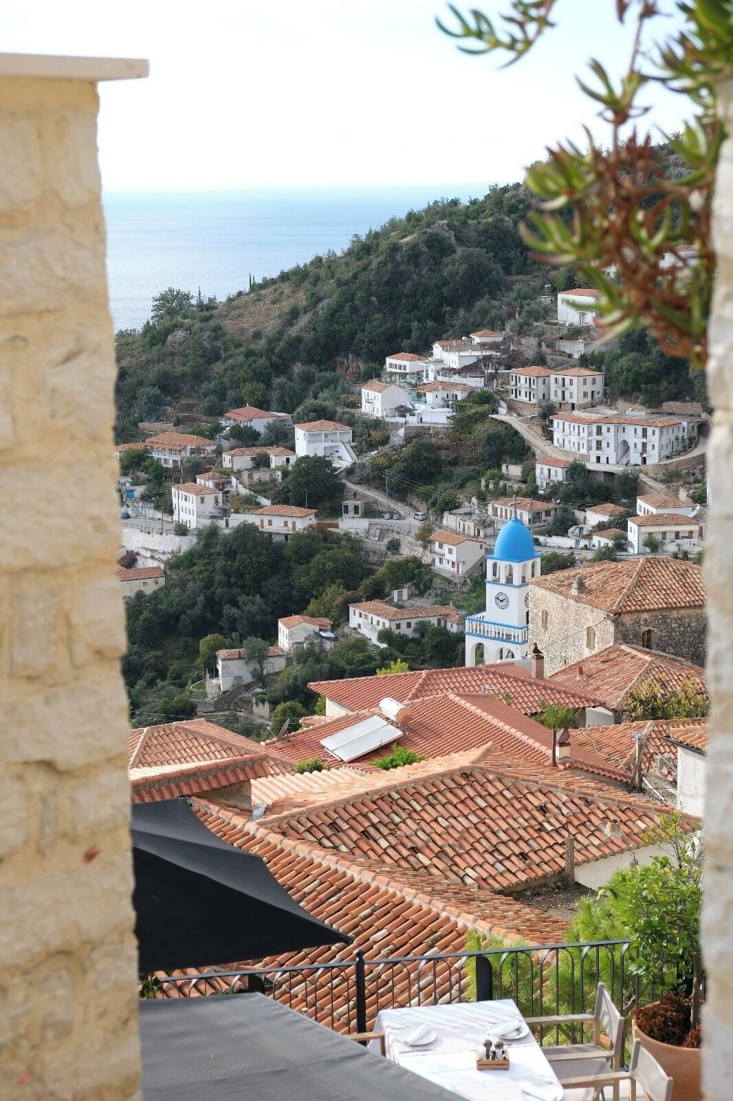 A coastal village with terracotta-roofed buildings, a prominent clock tower, and a view of the sea.