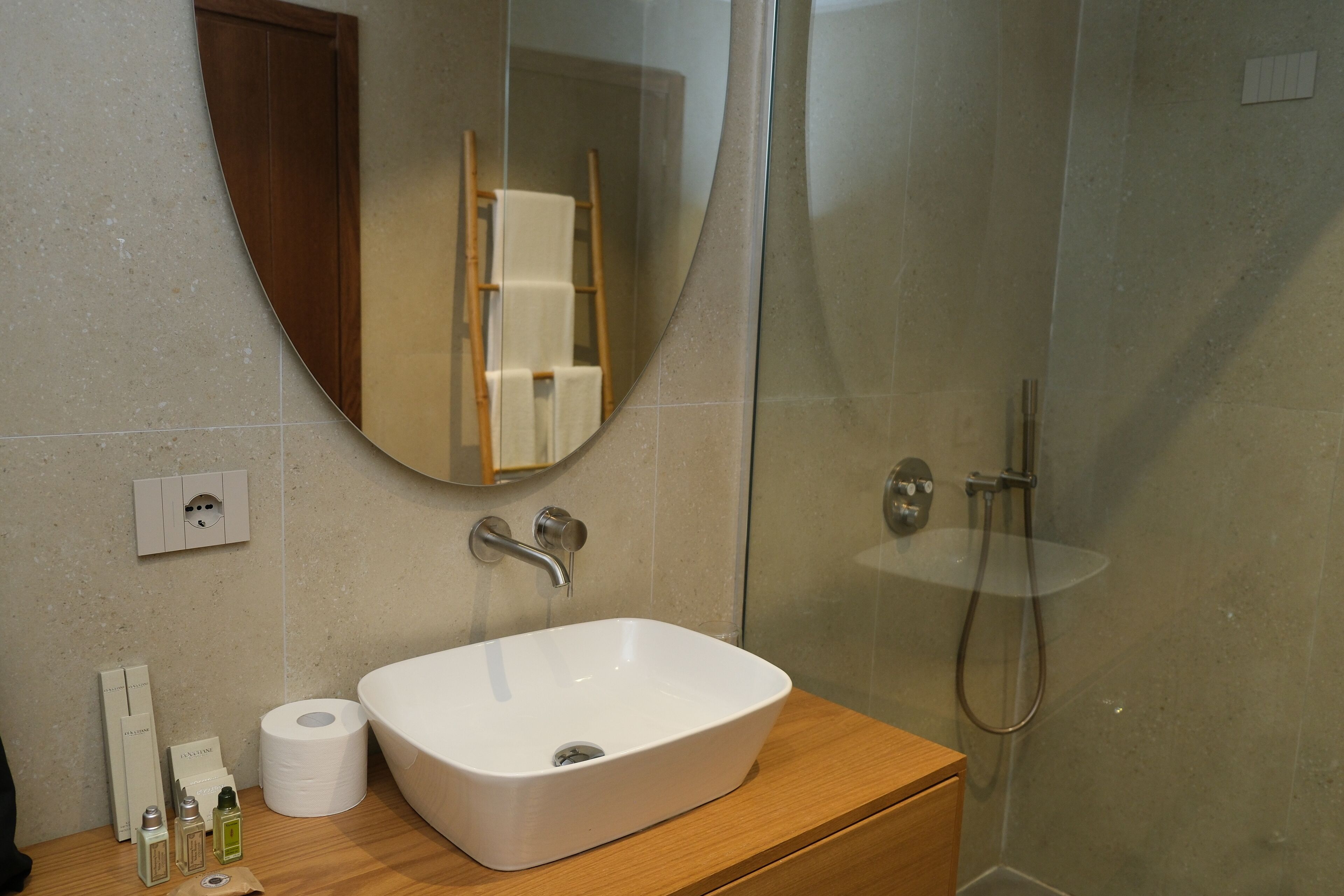 Ein Badezimmer mit einem weißen Waschbecken, einem Spiegel, einer Dusche und Pflegeprodukten auf der Ablagefläche.