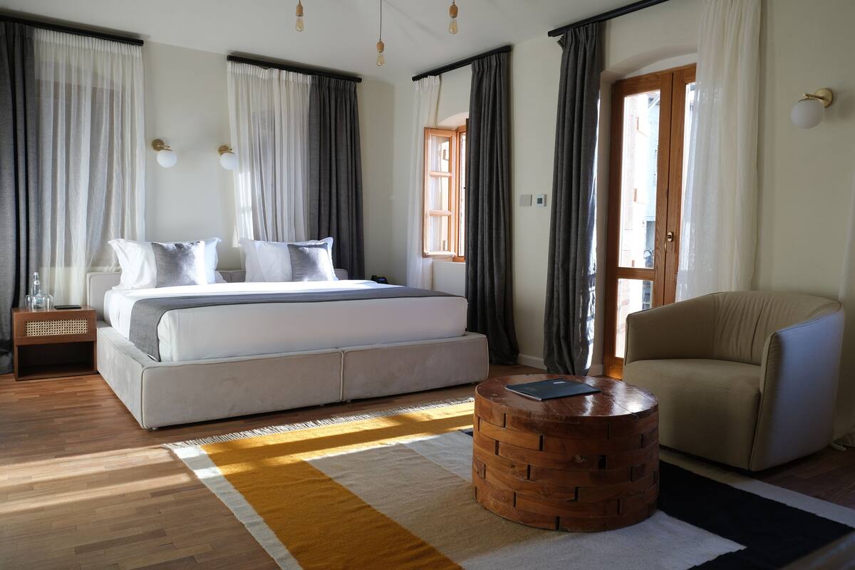 A bedroom with a large bed, a wooden side table, a round coffee table, and a beige armchair.