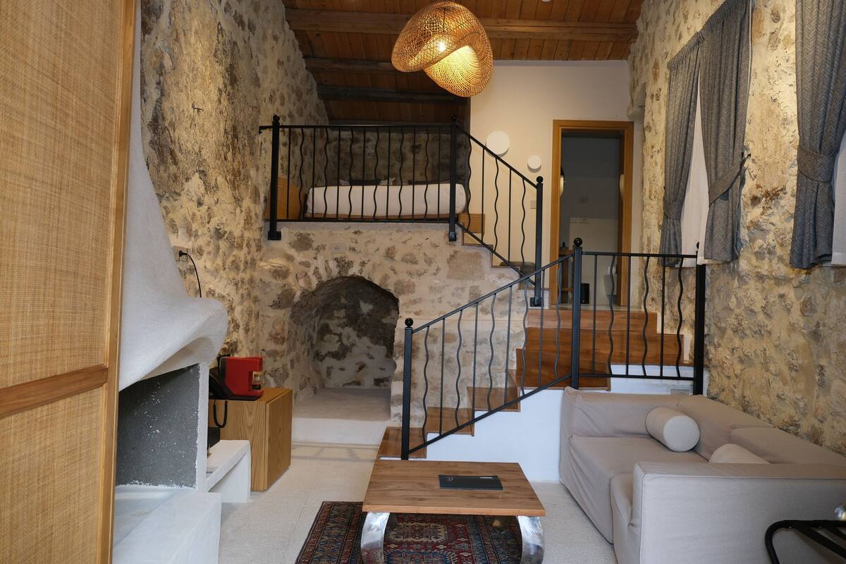 A cozy living room with a stone wall, a wooden staircase, a white sofa, and a woven light fixture.