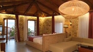 Un'ampia stanza con un letto grande, una poltrona e un'area pranzo. Presenta una parete in pietra e vista sull'esterno.