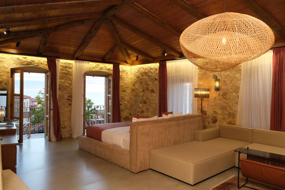 A spacious room with a large bed, a sofa, and a dining area. There is a stone wall and a view of the outdoors.