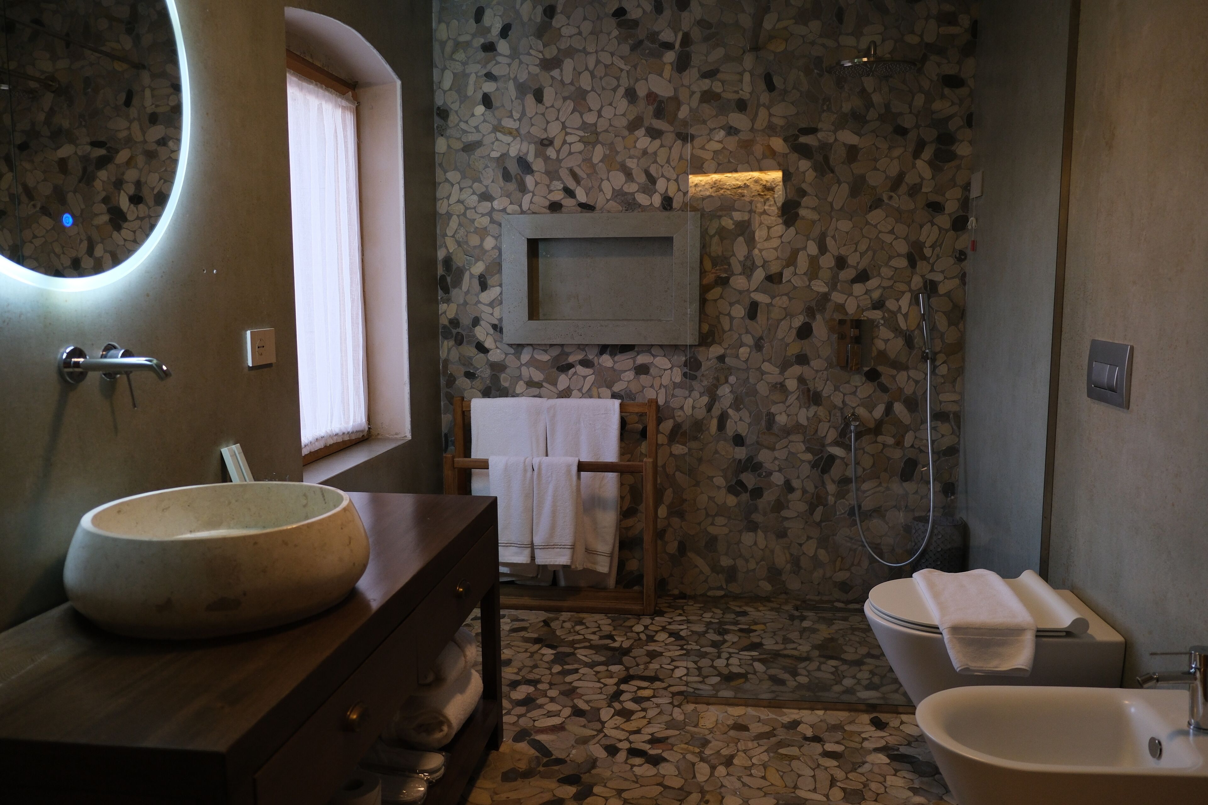 A bathroom with a round sink, a wooden vanity, a mirror, a framed picture, a towel rack, a shower, and a bathtub.