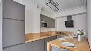Une cuisine moderne avec des meubles gris, un plan de travail en bois et un coin repas avec une table mise pour deux personnes.