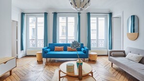 Un salon avec un canapé bleu, un canapé gris, une table basse ronde et un luminaire suspendu.