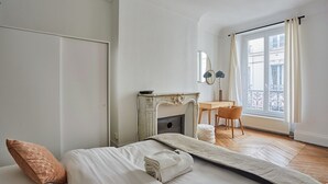 Une chambre à coucher avec un lit, une cheminée, un bureau et une fenêtre avec des rideaux.