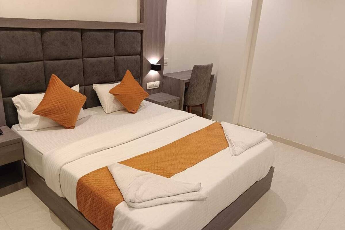 Una cama doble con cabecera gris, ropa de cama blanca y detalles naranja.