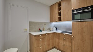 A compact kitchen with wooden cabinets, a built-in oven, and a white countertop. - Superb Apartment in the Heart of Paris (Paris)