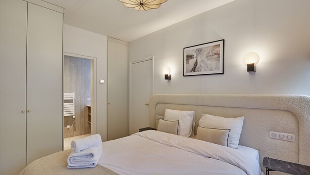 A neatly arranged bedroom with a large bed, a bedside table, a wardrobe, and a framed artwork on the wall. - Superb Apartment in the Heart of Paris (Paris)
