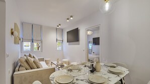 A dining area with a round table set for four, a sofa, and a television mounted on the wall. - Superb Apartment in the Heart of Paris (Paris)