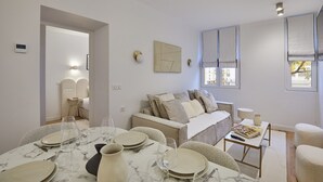 A modern, well-lit room with a dining table set for four, a sofa, and a window with blinds. - Superb Apartment in the Heart of Paris (Paris)