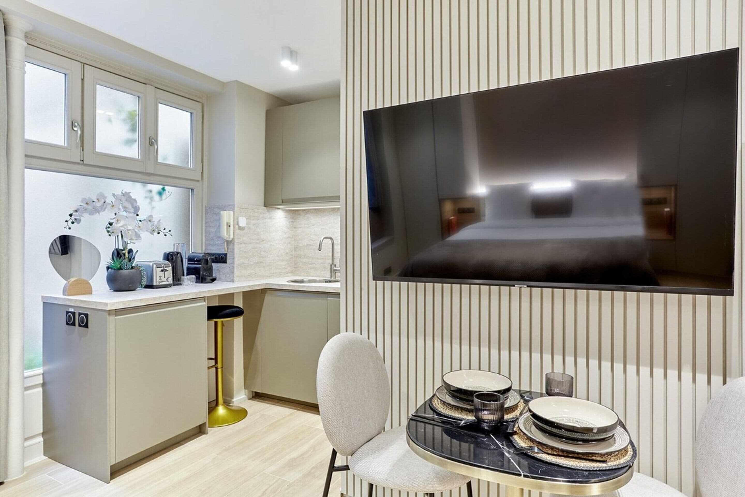 Eine moderne Küche mit Einbauofen, ein Essbereich mit rundem Tisch und ein großes Flachbildfernsehen an der Wand.