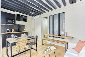 Una cocina moderna con gabinetes negros, un comedor con mesa y sillas de madera, y una zona de estar acogedora con un banco y un sofá blanco.