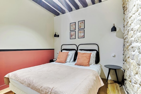 A bedroom with a bed, a nightstand, a wall-mounted lamp, and a small table. - Apartement Pantheon Ile Saint Louis 2 Bdrs (Paris)