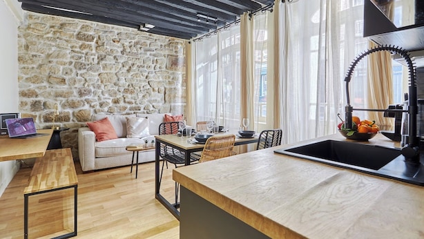 Un salon chaleureux avec un mur en pierre, un plancher en bois et un coin repas comprenant une table et des chaises.