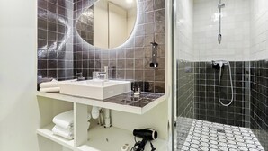 Une salle de bain moderne avec un grand miroir, un lavabo et un espace douche.