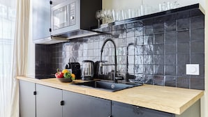 Une cuisine moderne avec des meubles de couleur noire, un plan de travail en bois, un évier noir et un revêtement mural en carreaux.