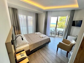 Habitación de hotel con cama, escritorio con teléfono, silla y balcón con vistas al mar.