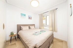 Un dormitorio con una cama, una mesita con una planta y una ventana con cortinas.