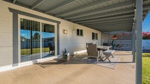 Ein überdachter Patio-Bereich mit Tisch und Stühlen, einem Blumentopf und Blick auf den Garten.