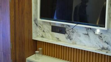 Televisão fixada numa parede de mármore com painel de madeira ao fundo.
