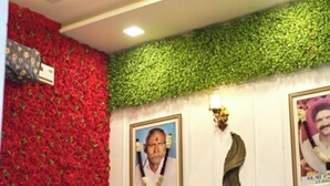 A living room with a red floral wall, a green leafy accent wall, a brown sofa, and a glass coffee table. - Hotel Mango Tree (Hansi)