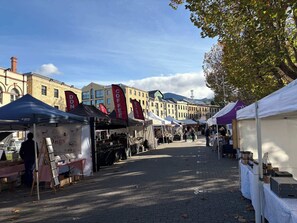 Une rue pavée bordée d’étals et de tentes de marché, avec des bâtiments en arrière-plan.