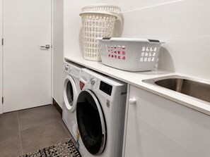 Un área de lavandería con una lavadora de carga frontal, un lavabo y dos cestos para ropa.