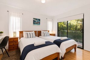 A hotel room with two beds, a desk, a chair, a small table with a plant, and a large window with a view of greenery. - The Tree House Hobart, Treetop Escape, Sleeps 8. (Taroona)