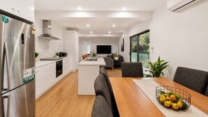 Een moderne keuken met een centraal eiland, een eetgedeelte met een houten tafel, en een woonkamer met een flatscreen-televisie.