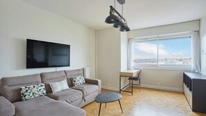 A modern living room with a sofa, a small table, and a TV mounted on the wall. - 2 Bedroom Flat Centre de Paris - Eiffel Tower View (Paris)