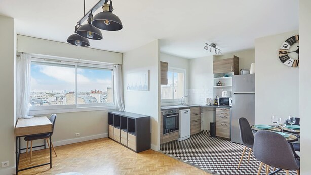 A modern kitchen with a black and white checkered floor, a dining area with chairs, and a view of the city through large windows. - 2 Bedroom Flat Centre de Paris - Eiffel Tower View (Paris)