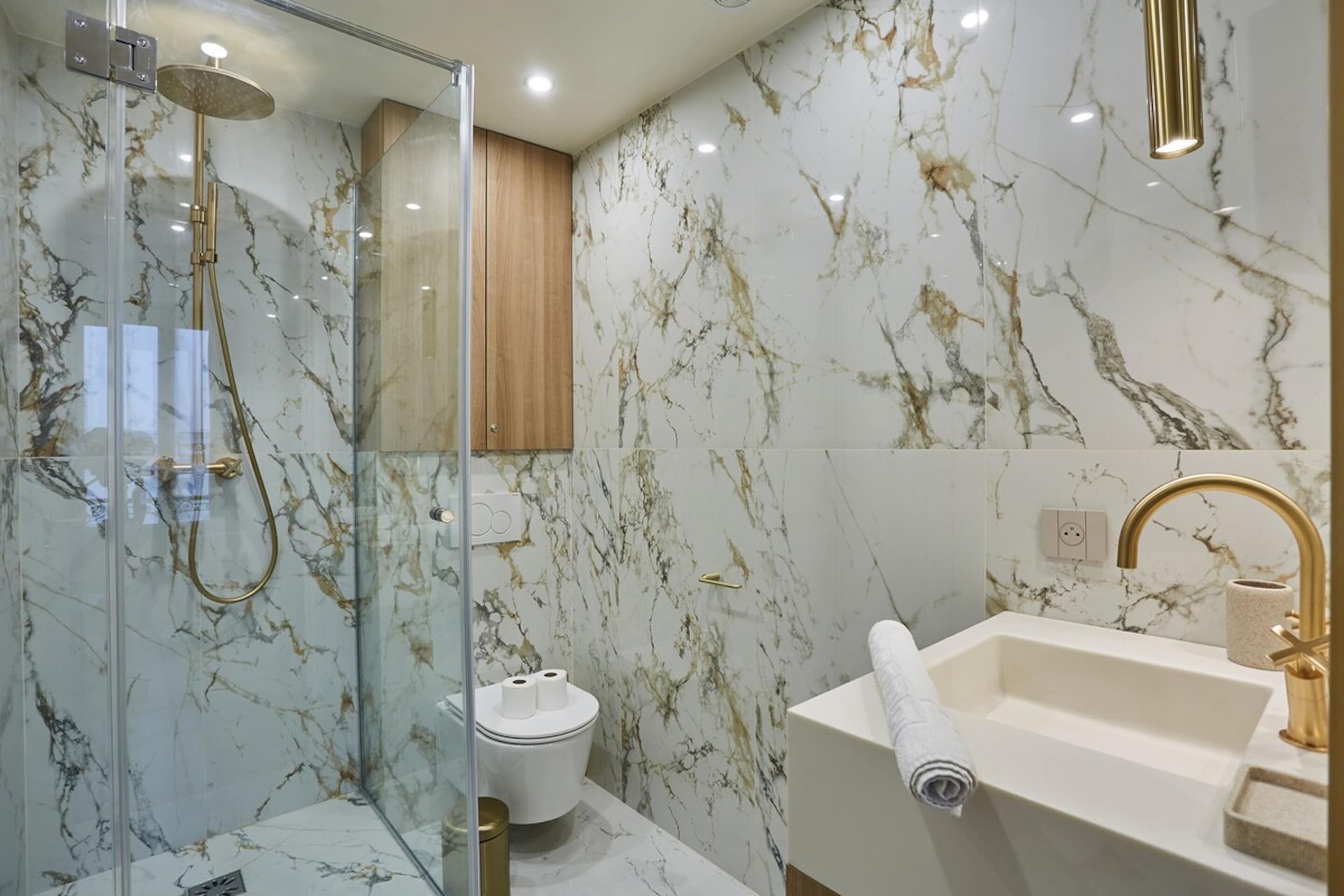Een badkamer met een douche met glazen wand, een toilet en een wastafel met een gouden kraan.