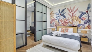 Un dormitorio con cama, un mural floral grande, una puerta corrediza y un separador de ratán.
