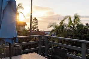 A balcony with wicker chairs, overlooking a tropical landscape with palm trees and a view of the sea. - Ocean View Deck! | Walk to the Beach | King Suite (Encinitas)