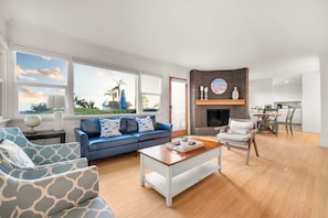 A spacious living room with a blue sofa, a coffee table, and a fireplace. - Ocean View Deck! | Walk to the Beach | King Suite (Encinitas)