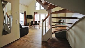 Ein großzügiger Wohnbereich mit einer Holztreppe zu einem Balkon, einem Essbereich und einer Küche.