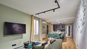 Un soggiorno moderno con una TV a schermo piatto, un divano, un'area pranzo con tavolo e sedie, e una scala che conduce a un altro livello.
