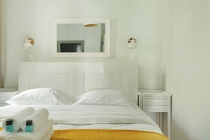 Een hotelkamer met een bed, een wit hoofdbord, twee nachtkastjes, een spiegel en twee wandlampen.