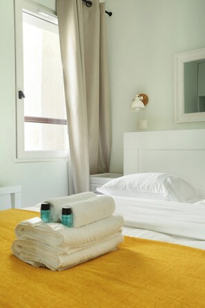 A neatly made bed with white linens and a yellow blanket, a window with beige curtains, and a bedside lamp. - Apartment Center of Paris (Paris)