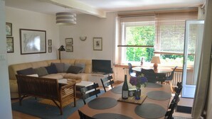 Una sala de estar con sofá, televisor, mesa de comedor, sillas y una ventana con persianas.