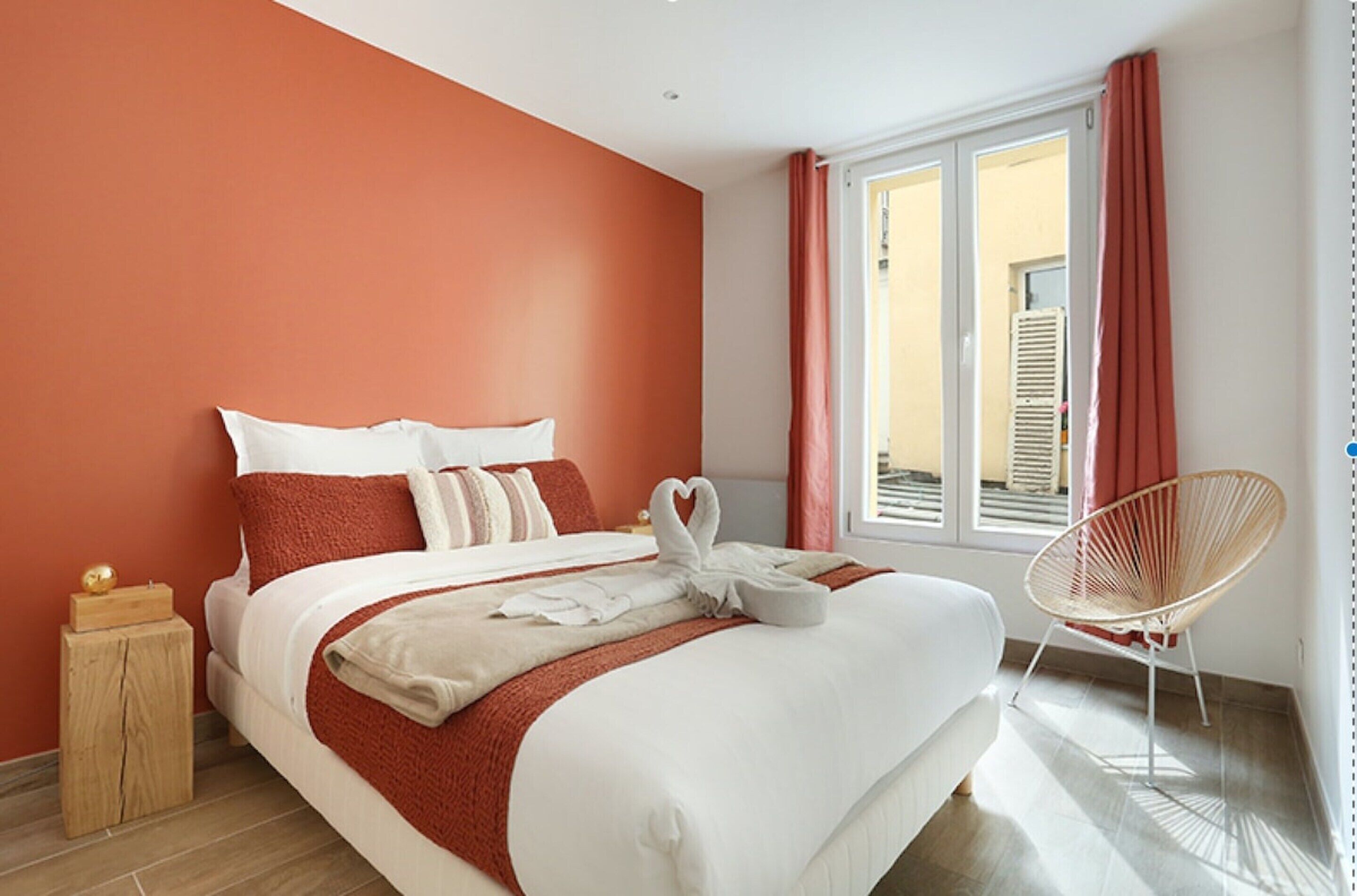 Une chambre d’hôtel avec un lit, une table de chevet en bois, une chaise en osier et une fenêtre avec des rideaux.