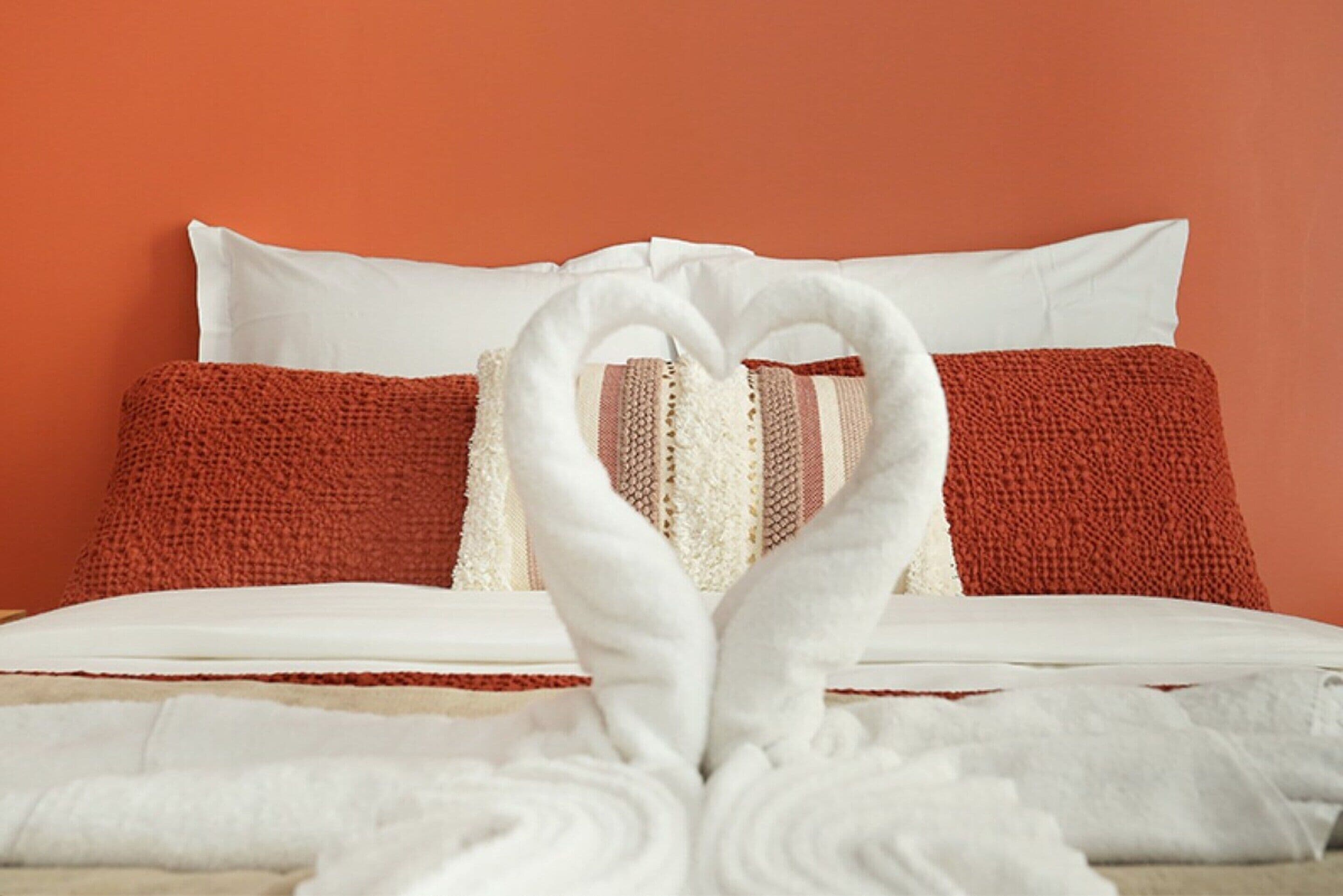 Ein Bett mit weißen und roten Kissen, einer weißen Decke und einem Handtuch, das zu einem Herzen geformt ist.