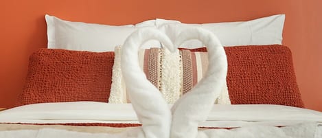 Ein Bett mit weißen und roten Kissen, einer weißen Decke und einem Handtuch, das zu einem Herzen geformt ist.